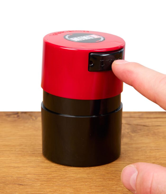 Finger drückt auf den Druckknopf eines roten Tightvac MINIVAC Vakuum-Containers auf Holzoberfläche.