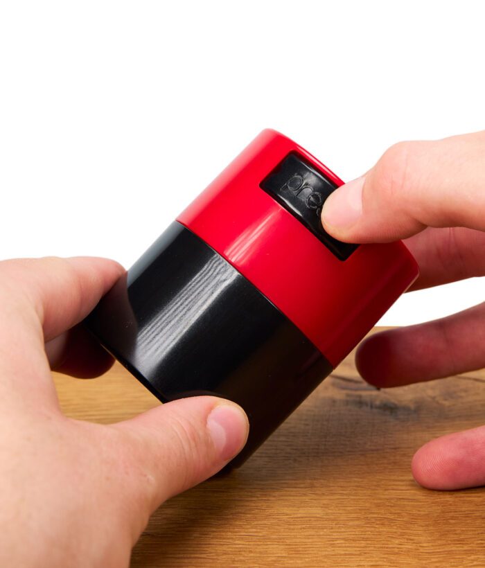 Roter Tightvac MINIVAC Vakuum-Behälter mit Druckverschluss in Nahaufnahme, wird von zwei Händen geöffnet.
