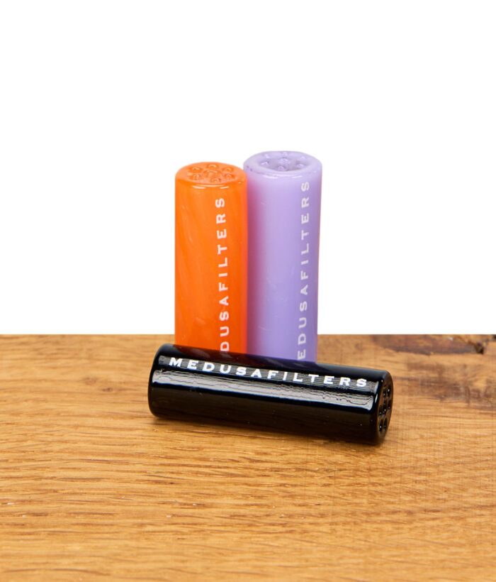 Drei Medusafilters Glasfilter in Orange, Lila und Schwarz auf Holzfläche, schwarzer Filter liegt vorne