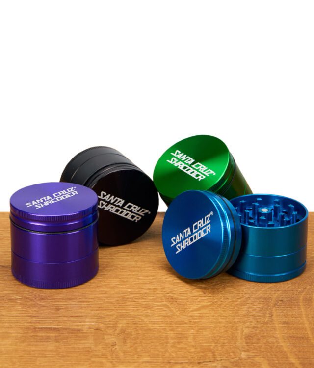 Vier dreiteilige Santa Cruz Shredder Grinder in verschiedenen Farben, einer geöffnet mit sichtbaren Mahlzähnen