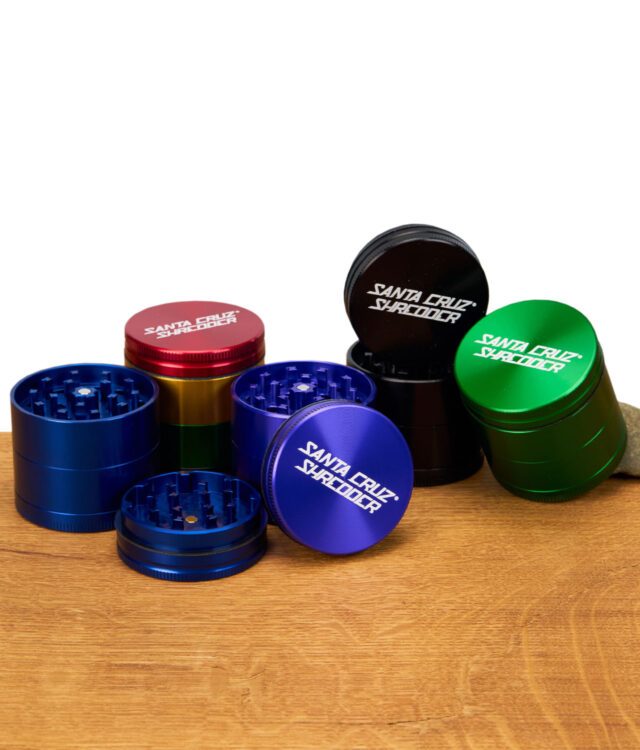 Mehrere vierteilige Santa Cruz Shredder Grinder in verschiedenen Farben, teils geöffnet mit sichtbarem Mahlwerk