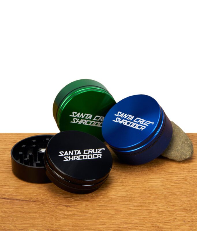 Drei zweiteilige Santa Cruz Shredder Grinder in Schwarz, Blau und Grün auf Holzuntergrund