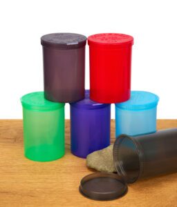 Bunte Aufbewahrungsdosen mit Pop-up-Deckel in Pyramidenform, eine Dose geöffnet und liegend auf einem Stein.