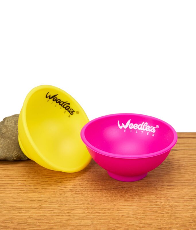 Zwei bunte Weedlez Mischschalen aus Silikon in Pink und Gelb auf Holzuntergrund