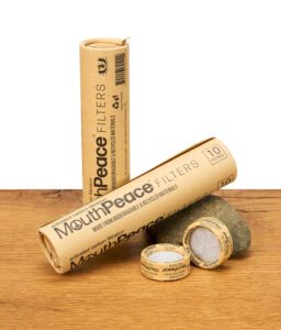 Verpackung und mehrere MouthPeace Filter liegen dekorativ auf einem Holztisch vor einem Stein.