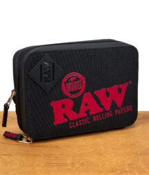 Schwarze RAW Weekender Travel Bag mit rotem Logo und goldfarbenem Reißverschluss auf Holztisch