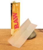 Geöffnetes Päckchen RAW Ethereal Paper mit einem herausgezogenen, extrem dünnen Blatt auf einem Stein