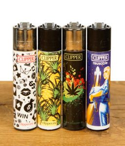 Vier Clipper-Feuerzeuge mit unterschiedlichen Motiven wie Ananas, Hanfblatt und Spielsymbolen, aufrecht nebeneinander aufgestellt auf Holzfläche.