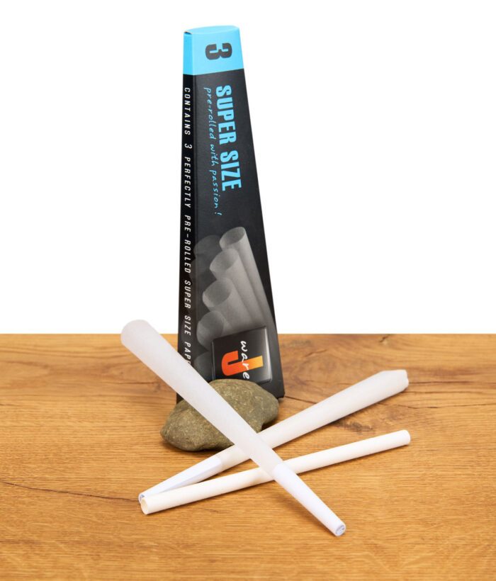 Drei ungefüllte Super Size Cones von JWare vor der aufrecht stehenden Verpackung auf einem Holztisch