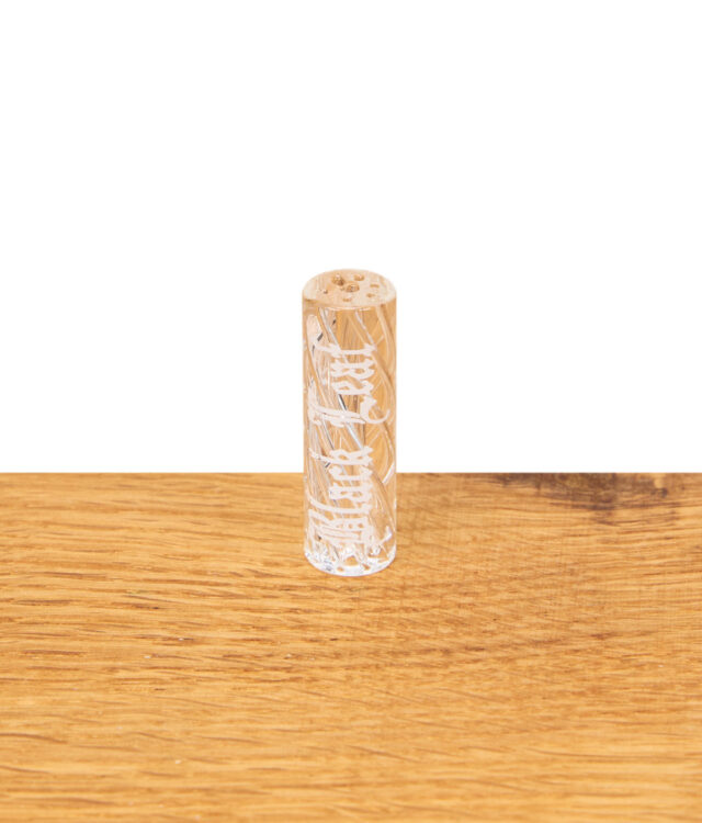 Black Leaf Glasfilter mit 9 mm Durchmesser, stehend auf einem Holztisch, zeigt die feine weiße Gravur im Glasdesign