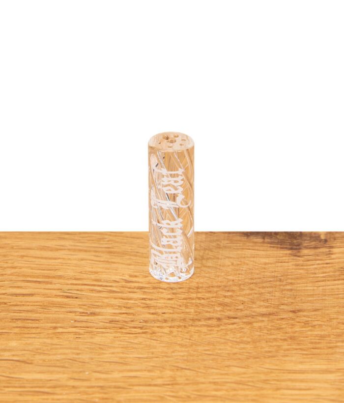 Black Leaf Glasfilter mit 9 mm Durchmesser, stehend auf einem Holztisch, zeigt die feine weiße Gravur im Glasdesign