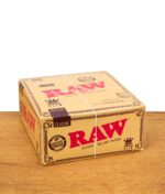 Geschlossene Box mit 50 Packungen RAW Classic King Size Slim Papers auf Holzuntergrund