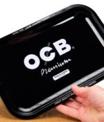 OCB Premium Rolling Tray wird an einer Ecke mit der Hand hochgehalten, leicht schräg auf einem Holztisch.