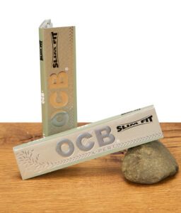 Zwei OCB X-PERT Slim Fit Booklets auf Holzuntergrund, eines stehend, eines liegend mit silbernem Logo