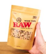 Hand hält eine geöffnete Packung RAW Wide Tips mit sichtbarem Inhalt.