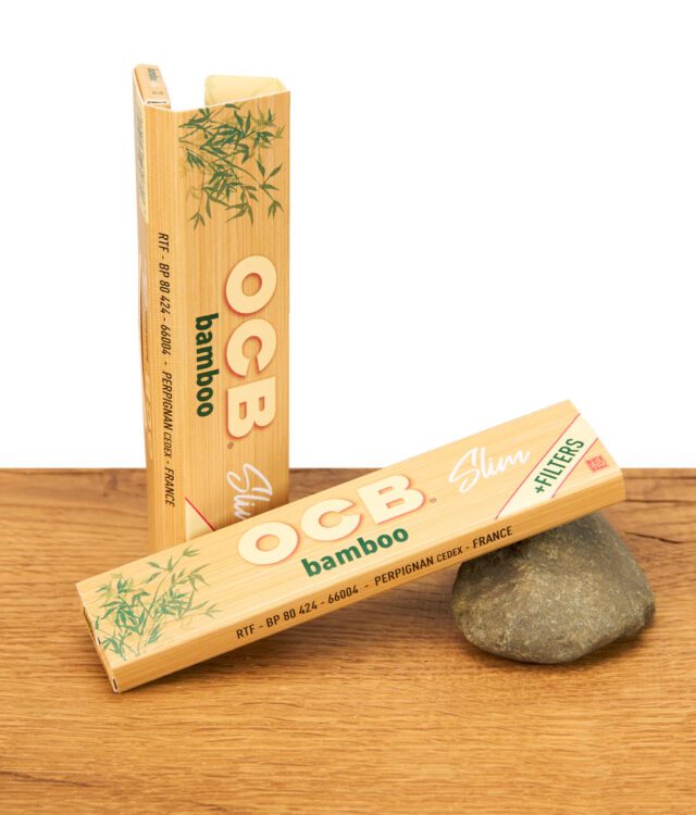 Zwei geschlossene OCB Bamboo Slim Packungen mit Bambusdesign auf Holzuntergrund, eine aufrecht stehend und eine liegend.