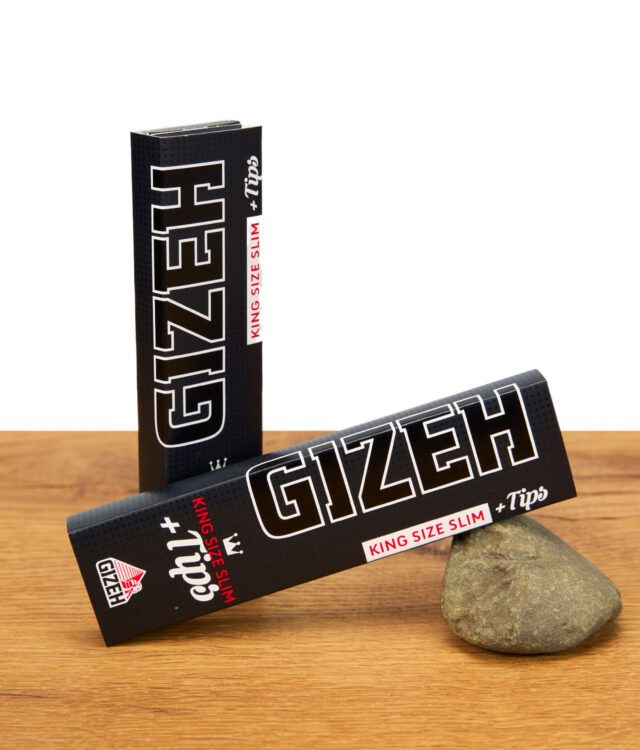 Zwei Gizeh King Size Slim +Tips Paperpacks, eines stehend und eines schräg an einem Stein gelehnt