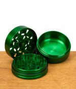 Geöffneter grüner Grinder mit allen drei Teilen sichtbar auf Holzfläche