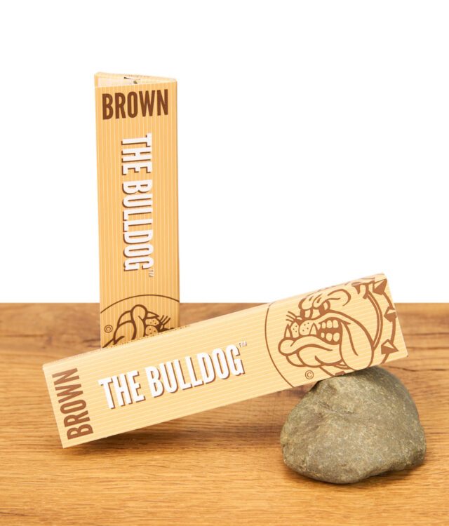 Zwei Packungen The Bulldog Brown Papers King Size Slim, eine stehend, eine liegend auf einem Stein