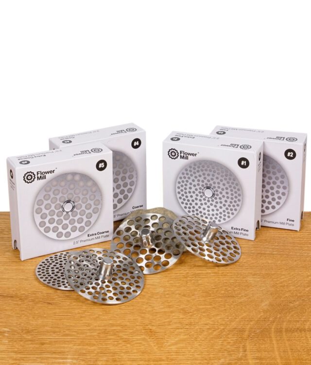 Flower Mill Milling Plates Set in allen vier Varianten (Extra Fine, Fine, Coarse, Extra Coarse) mit Verpackung auf Holzoberfläche.