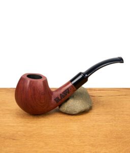 RAW Holzpfeife mit gebogenem schwarzem Mundstück, graviertem RAW-Logo, die auf einem Stein auf einem Holztisch ruht.