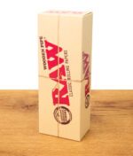 Aufrecht stehende Pappverpackung mit rotem RAW Aufdruck auf einem Holzbrett