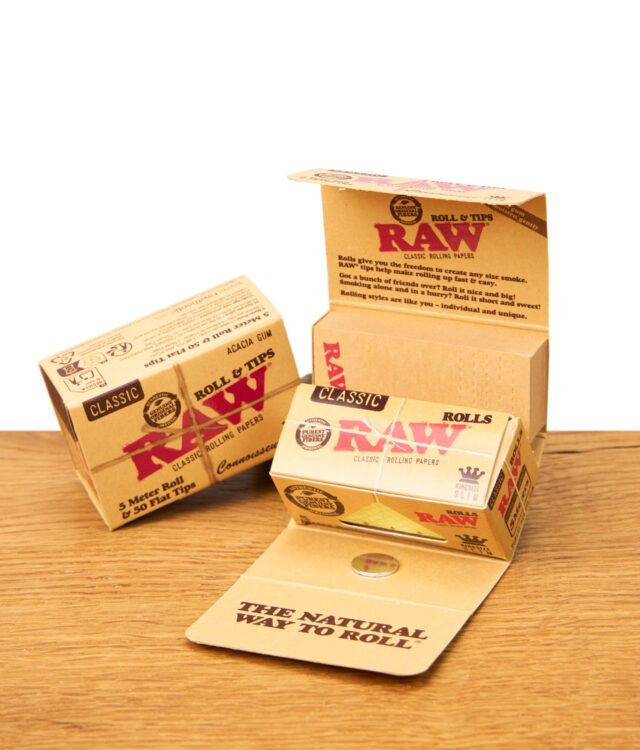 Zwei geöffnete RAW Connoisseur Rolls & Tips Classic Boxen mit sichtbarem Innenleben und Text, daneben eine geschlossene Box, alles auf einem Holztisch.