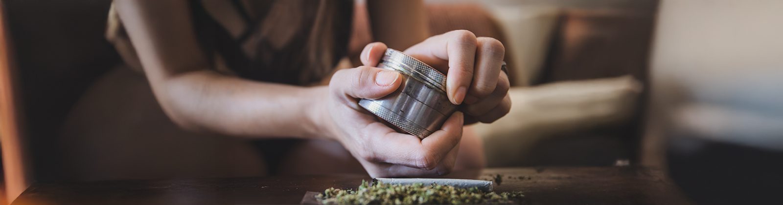 grinder klemmt und frau versucht diesen zu öffnen. Darunter liegt ein Joint bereit