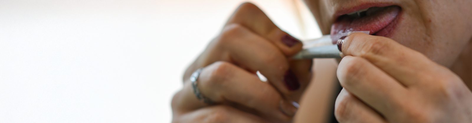 Frau mit lackierten Fingern und Ring benetzt die Klebefläche eines Drehpapiers mit der Zunge – Papers kleben nicht.
