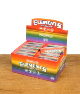Eine geöffnete Box mit mehreren bunten Verpackungen von Elements Rainbow Tips, auf einem Holztisch stehend. Das Elements-Logo ist gut sichtbar.