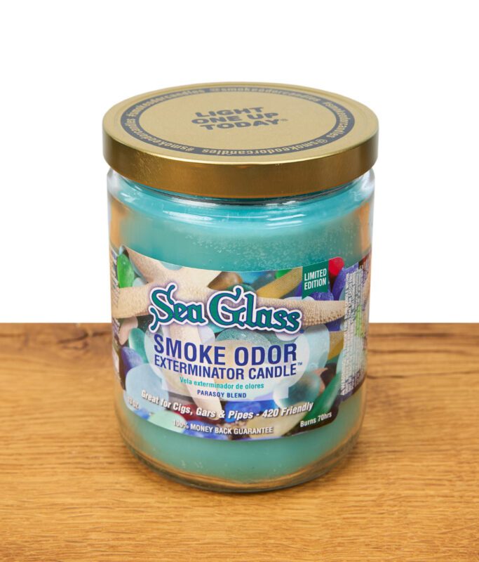 Die türkise Duftkerze "Sea Glass" mit buntem Aufdruck steht auf Holz präsentiert