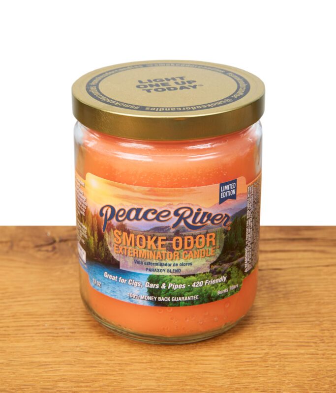 Orangene Duftkerze Peace River auf Holz platziert. Bunter Aufdruck auf der Kerze,