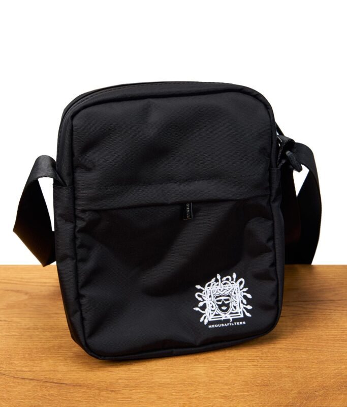 Schwarze Umhängetasche mit verstellbarem Gurt und weißem Medusafilters-Logo, stehend auf einem Holztisch.