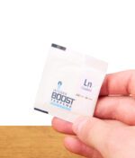 Hand hält einen kleinen weißen Feuchtigkeitsregulierer mit Ln Linalool Aufdruck über Holzoberfläche.