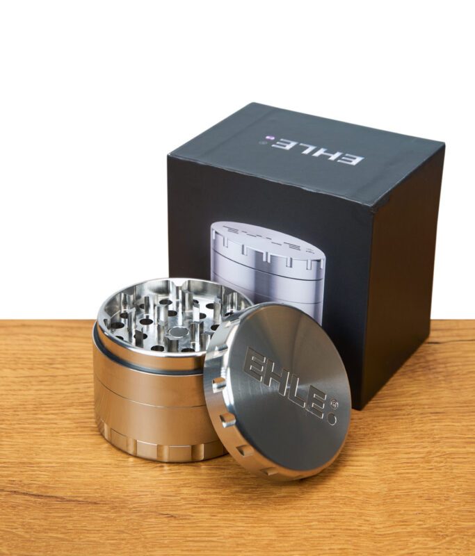 EHLE Edelstahl Grinder geöffnet vor schwarzer Verpackung mit Produktabbildung, auf Holztisch.