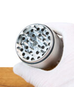 Edelstahl Grinder von EHLE wird mit weißem Handschuh gehalten, Fokus auf Mahleinheit, Holztisch im Hintergrund.