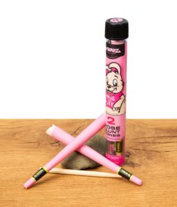 G-Rollz Rose Blunt Cones King Size, zwei pinke Blunt Cones und Verpackung mit Cartoon-Design auf Holztisch – aromatisierte King Size Cones, unverwechselbares Zubehör für Selbstgedrehte.