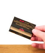 Hand hält offene RAW Black Classic Rolling Papers 1 1/4 Size, mit Einblick auf die ungebleichten Blättchen.