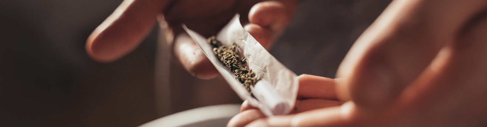 Dein Joint Filter fällt heraus? Zwei Hände halten Drehpapier mit Tabak gefüllt und der Filter liegt am Rand. Dunkler Hintergrund.