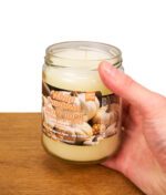 Hand hält weiße Duftkerze White Pumpkin von Smoke Odor vor weißem Hintergrund auf Holz