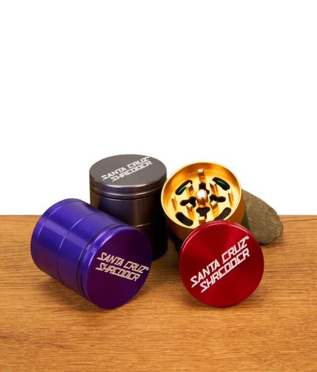 Santa Cruz Shredder Grinder 4-teilig 40 mm in Rot, Grün, Gold und Schwarz mit Sicht auf Sieb und Mahlwerk auf Holztisch