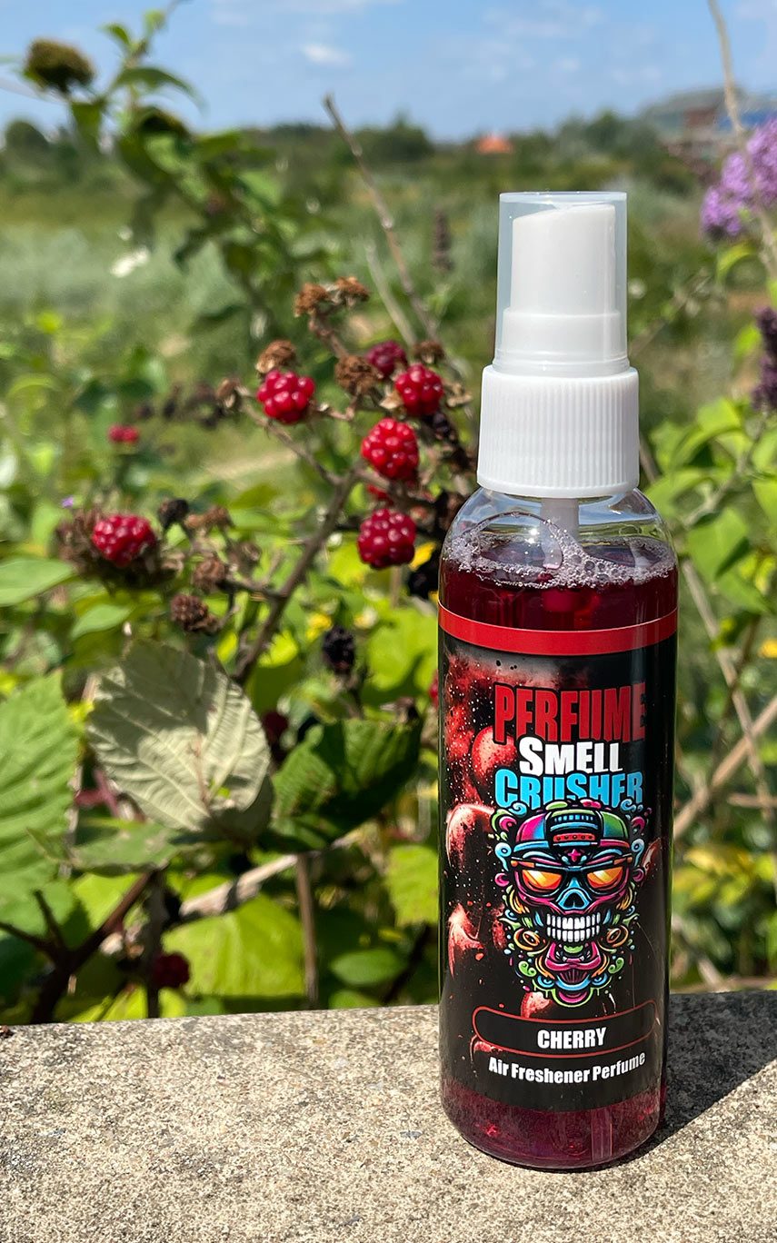 Das SmellCrusher Parfüm Cherry auf einer Steinkante vor grünen Pflanzen & einem Brombeer-Strauch platziert.