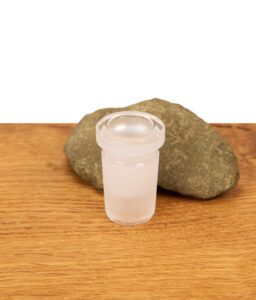 Einzeln stehender Bongadapter bzw. Schliffreduzierer aus Glas NS19 auf NS14 vor einem Stein auf Holz