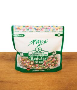 Geschlossene grüne Purize 50er Pack Regular Size Verpackung mit buntem Aktivkohlefilter-Design steht aufrecht auf einer Holzoberfläche vor weißem Hintergrund.