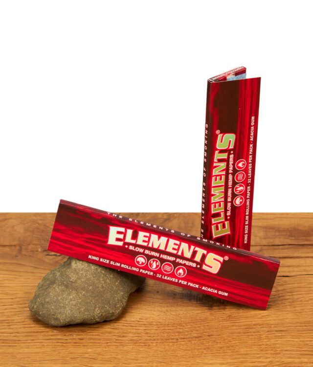 Zwei Packungen Elements Red Slow Burn Hemp Papers King Size Slim stehend und liegend auf einem Dekostein