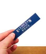 Ein dunkelblaues Heftchen Elements Phantom King Size Slim mit silberner Prägung wird zwischen Daumen und Zeigefinger gehalten.