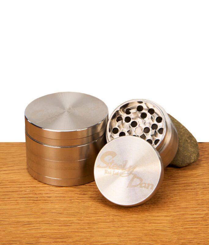 4-teiliger Steely Dan Edelstahlgrinder von Black Leaf in geöffnetem Zustand auf Holz, zeigt scharfe Mahlzähne und ein feines Pollensieb.