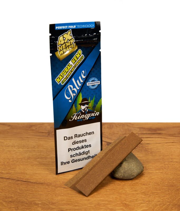 Kingpin Hemp Wraps Blue Packung mit zwei braunen, tabakfreien Hanf-Blättchen, die an einem Naturstein auf Holz lehnen.