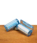 Elements Rolls King Size Nachfüllbox aus blauem Kunststoff und geöffnete Box mit eingelegter 5m Paper-Rolle auf Holzgrund.