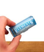 Eine Hand hält die geschlossene Elements Rolls King Size Nachfüllbox aus blauem, transparentem Kunststoff vor weißem Hintergrund.